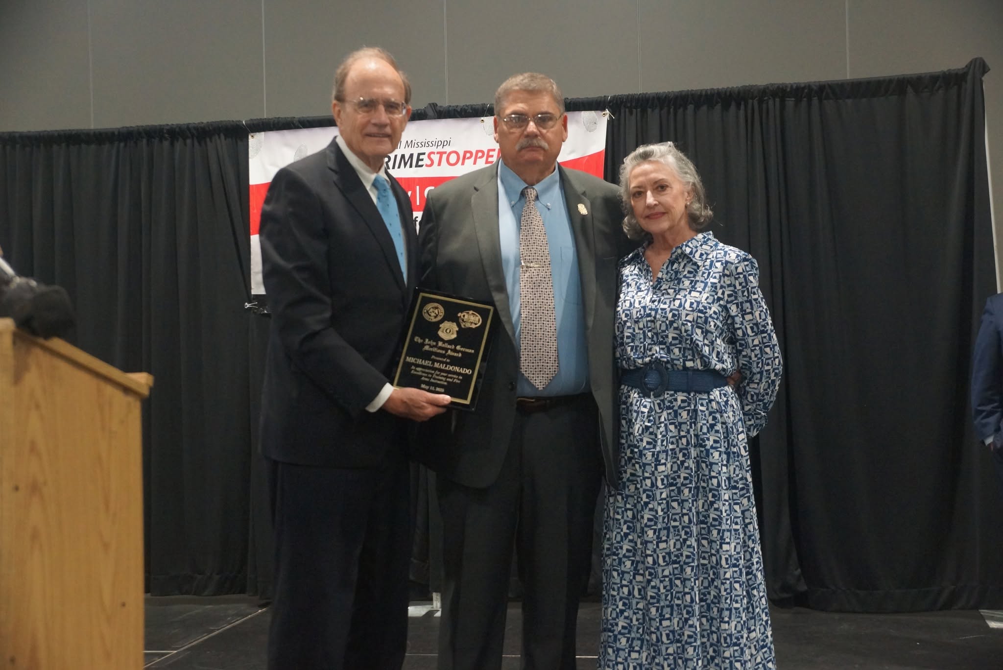 Award recipient holding a plaque with ceremony guests in 2025