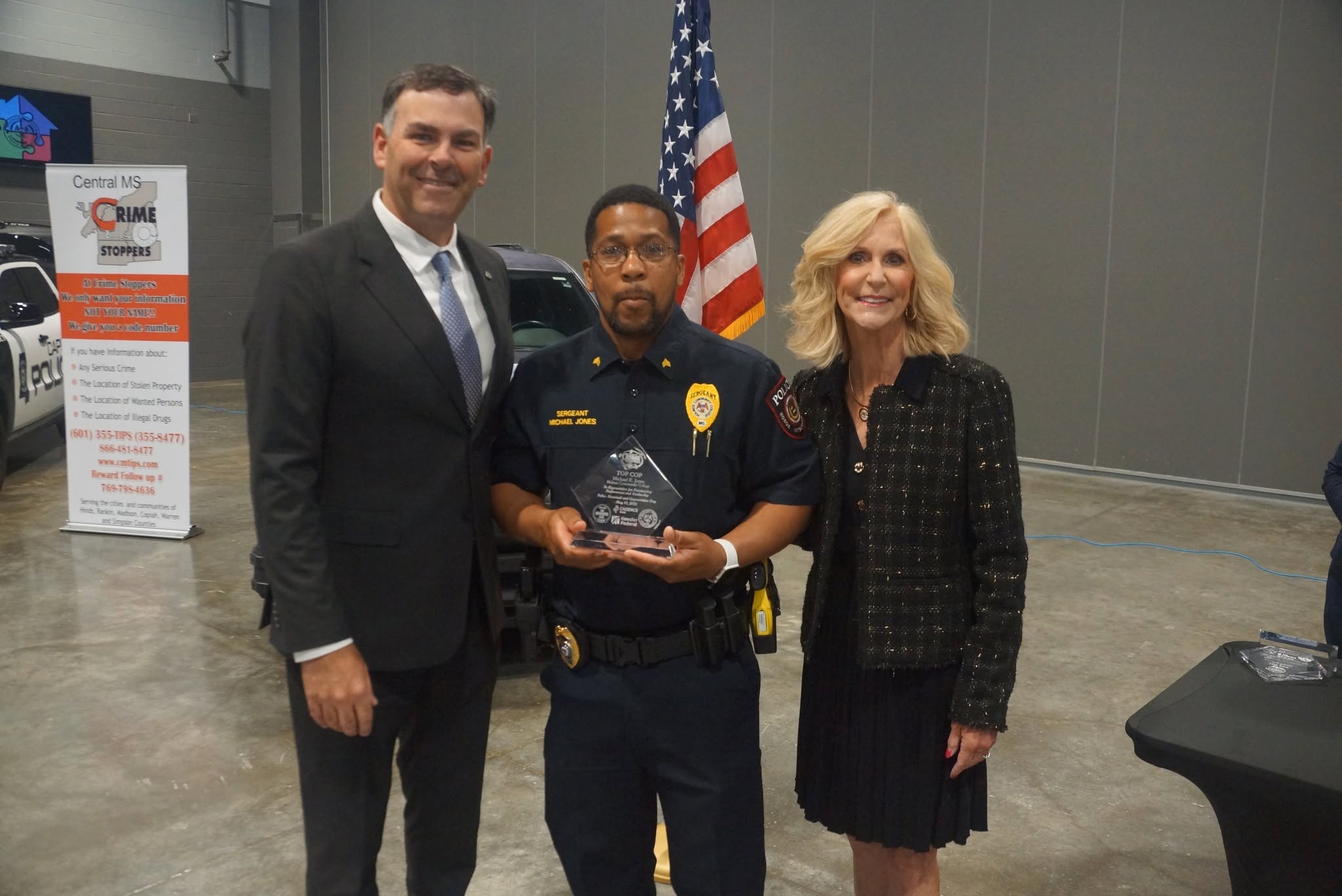 Uniformed officer holding an award with guests at the 2025 TOP COP ceremony