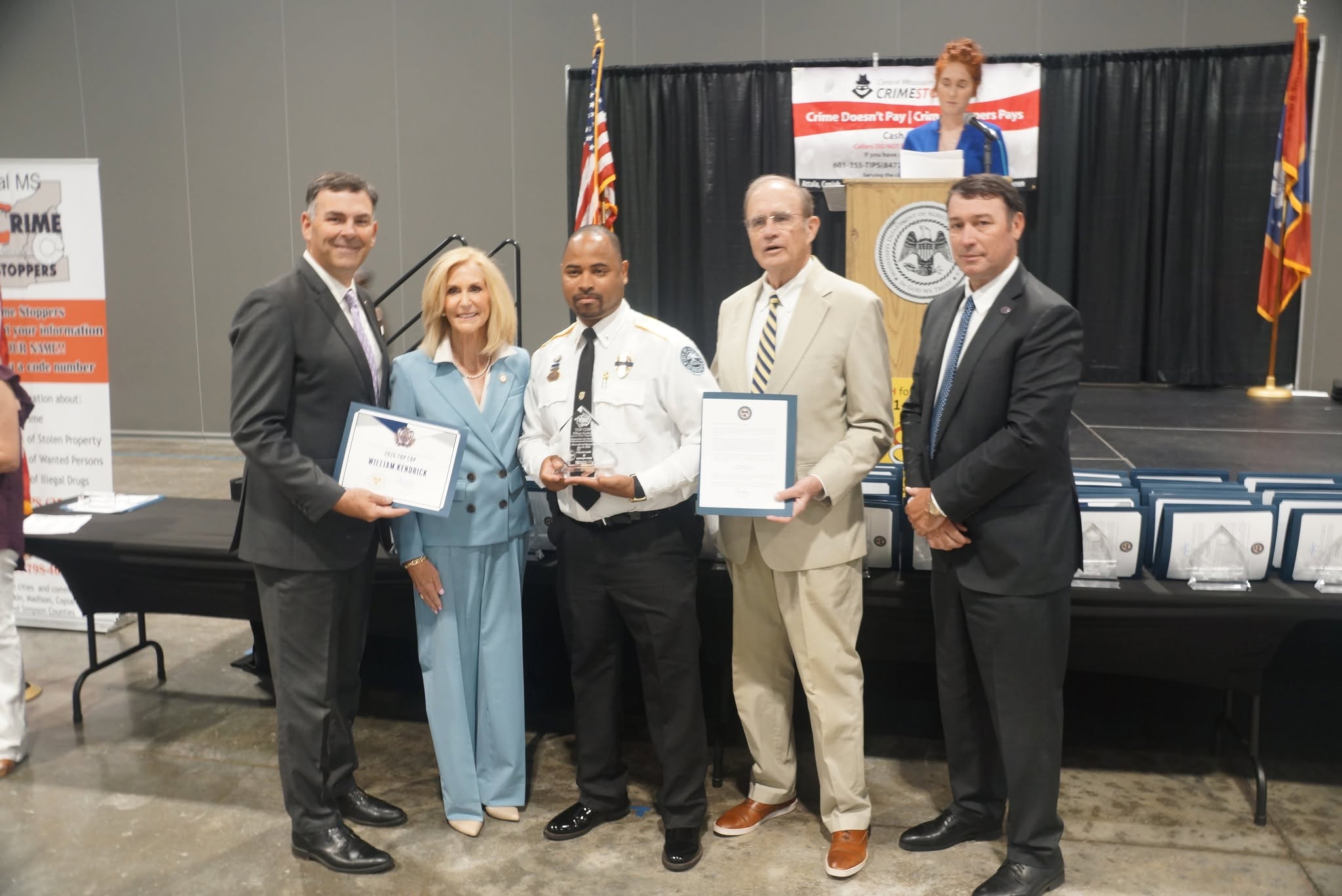Officer holding an award and certificates with guests at the 2026 TOP COP ceremony